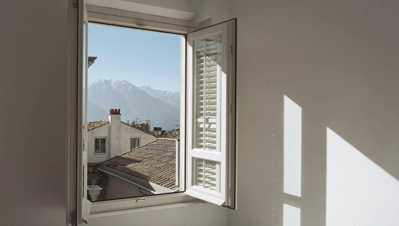 Fenêtre d’un appartement niçois un matin d’hiver, les Alpes enneigées au loin